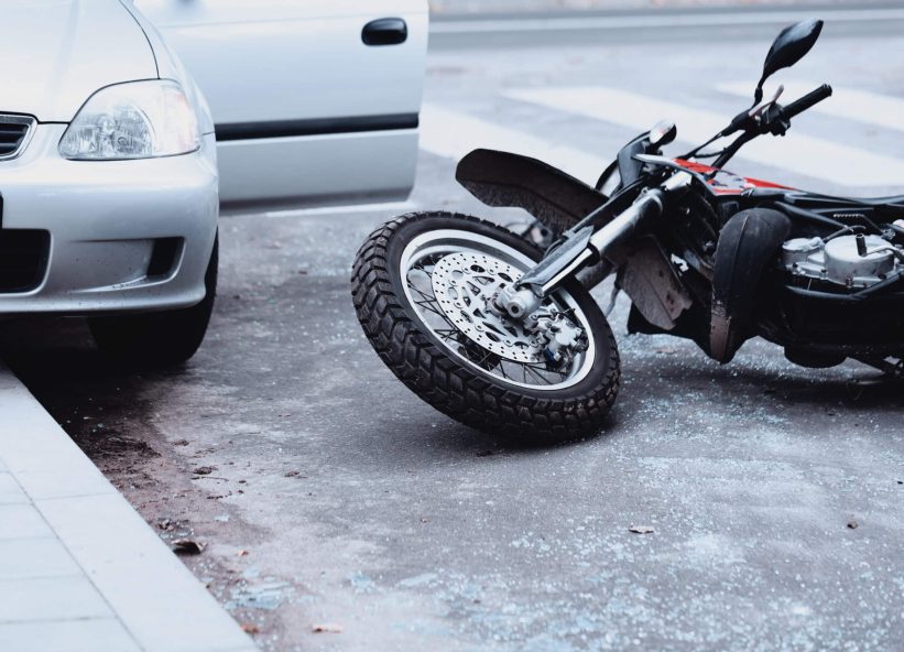 Motorcycle lying on the road and car standing with open door after a collision